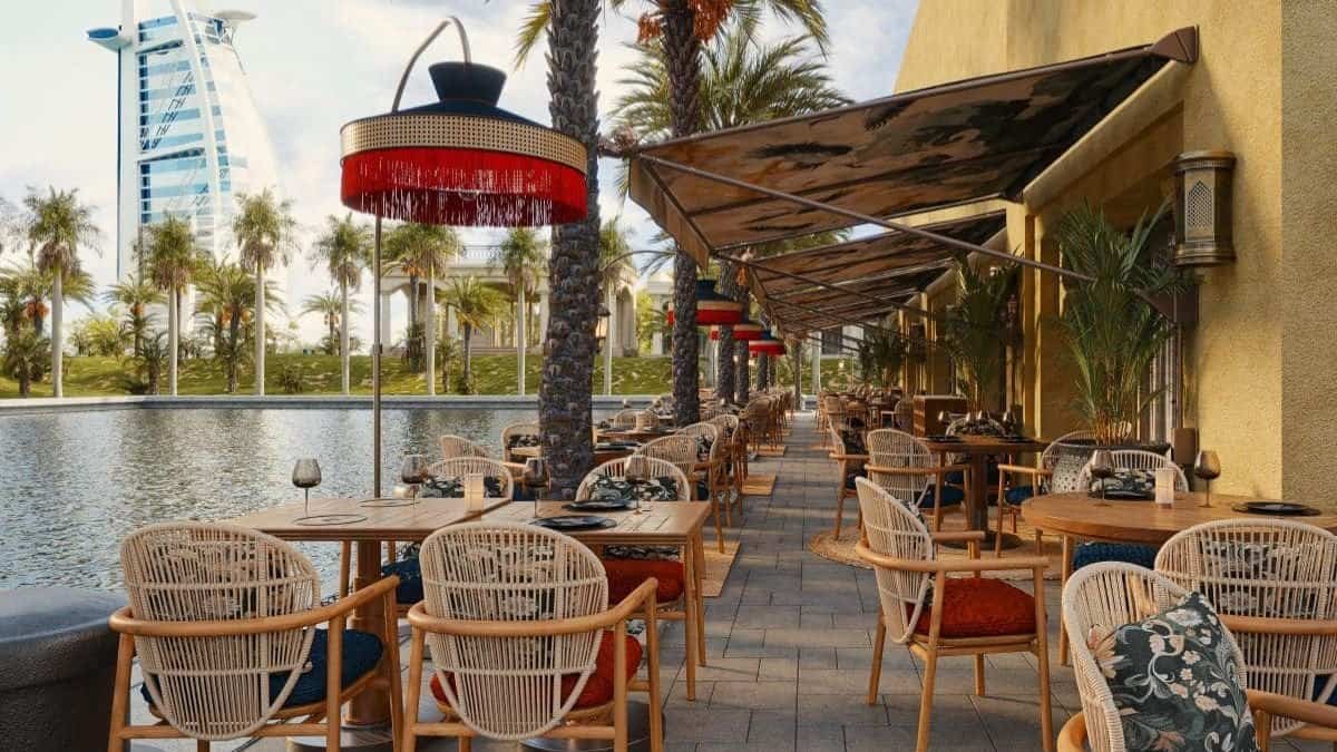 Outdoor dining area at Dubai restaurant with palm trees and water view.
