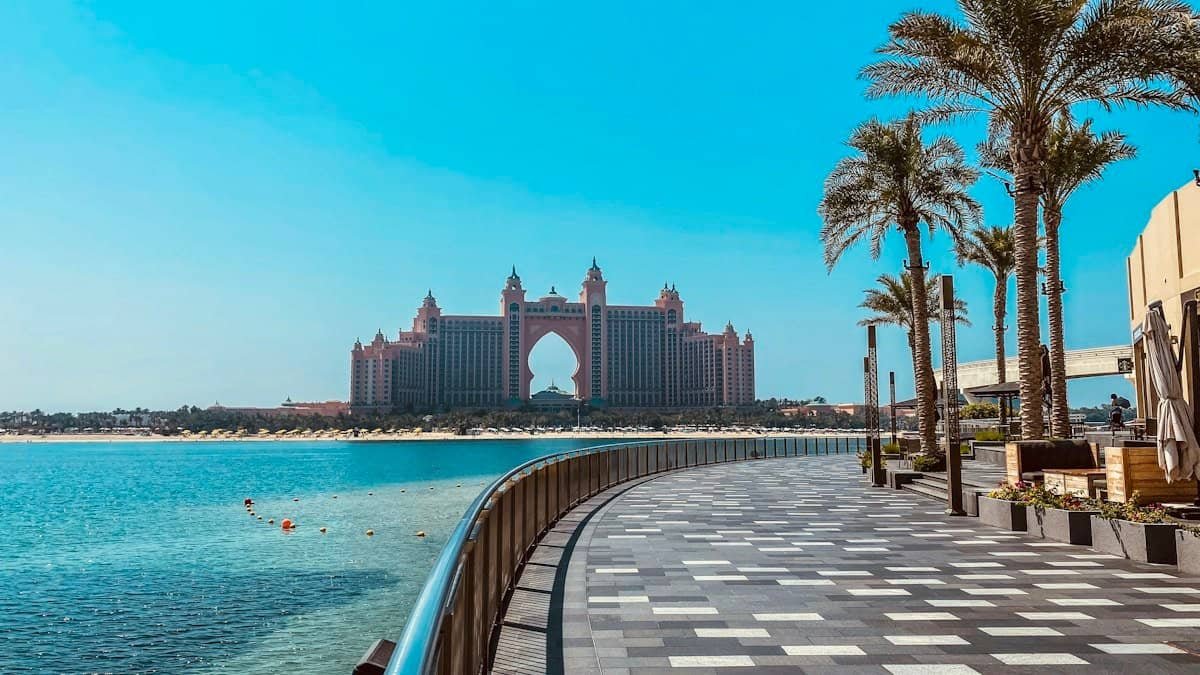 Atlantis The Palm seen across the water from a palm-lined boardwalk on Palm Jumeirah under a clear blue sky