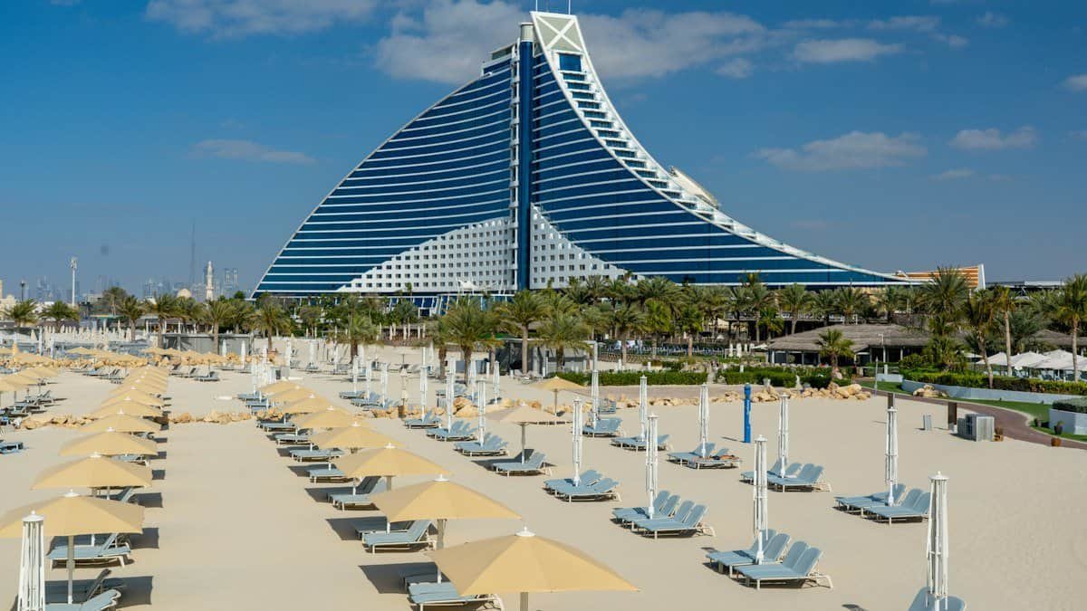 Rows of sunbeds and umbrellas on the private beach in front of the wave-shaped Jumeirah Beach Hotel