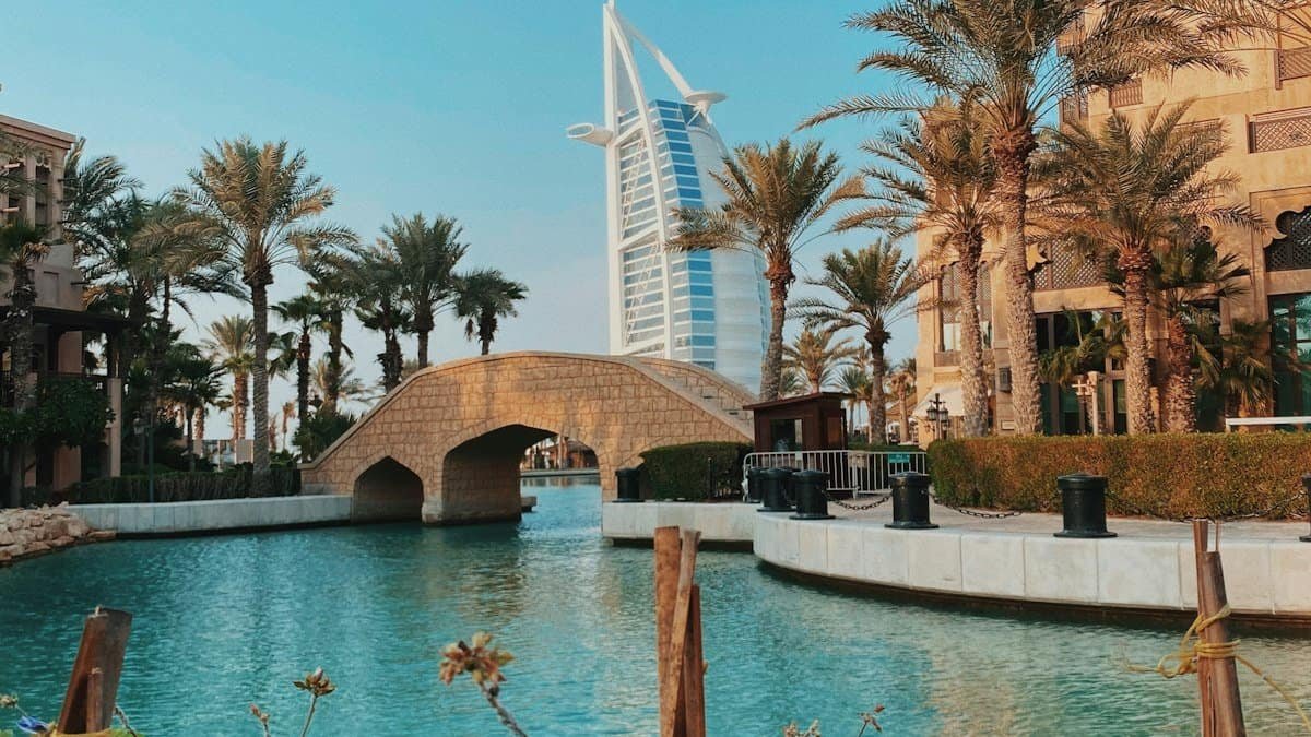 Palm-lined waterway and stone footbridge at Madinat Jumeirah with the Burj Al Arab rising behind