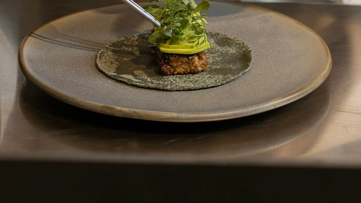Chef using tweezers to finish a tasting-menu course with micro herbs on a stoneware plate